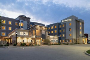 Un hotel de varios pisos con fachada de piedra, múltiples entradas y un estacionamiento.