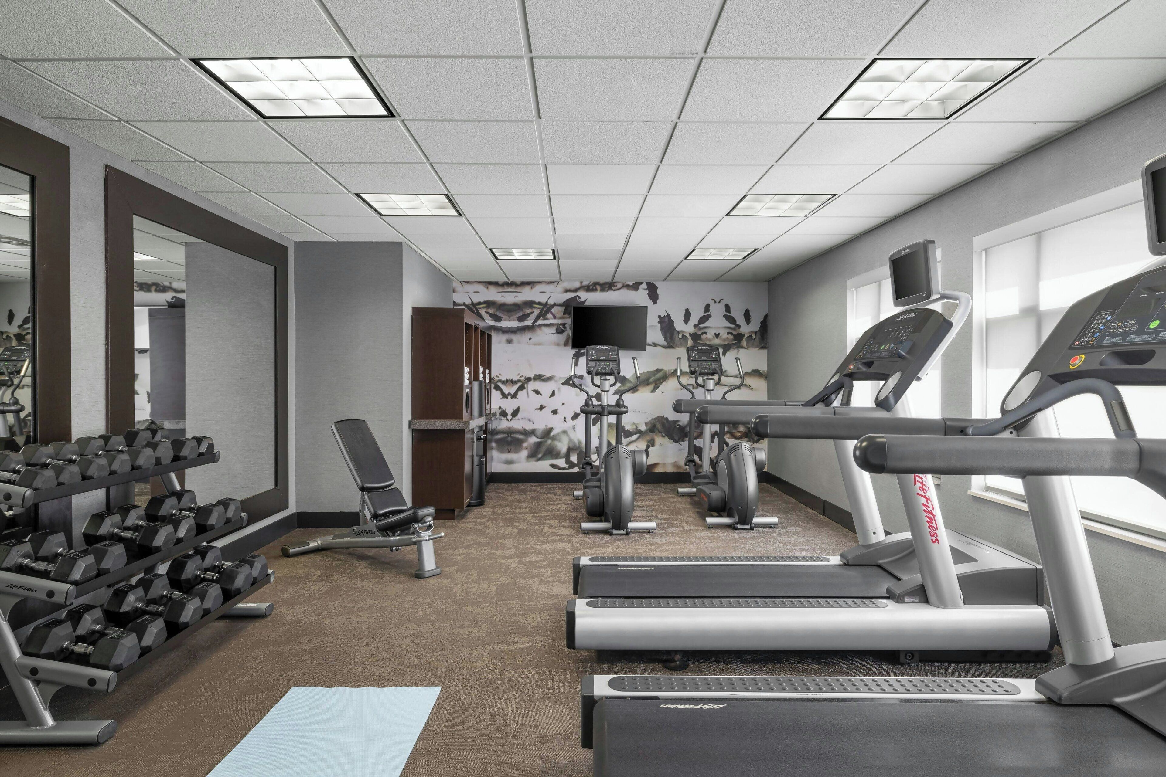 Une salle de sport équipée de tapis de course, de vélos elliptiques et d’haltères.