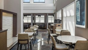 A modern hotel lobby with high ceilings, large windows, and a central seating area with tables and chairs. - Residence Inn Champaign (Champaign)