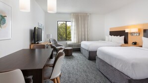 A hotel room with a desk, two beds, a TV, and a large window with curtains. - TownePlace Suites York (York)