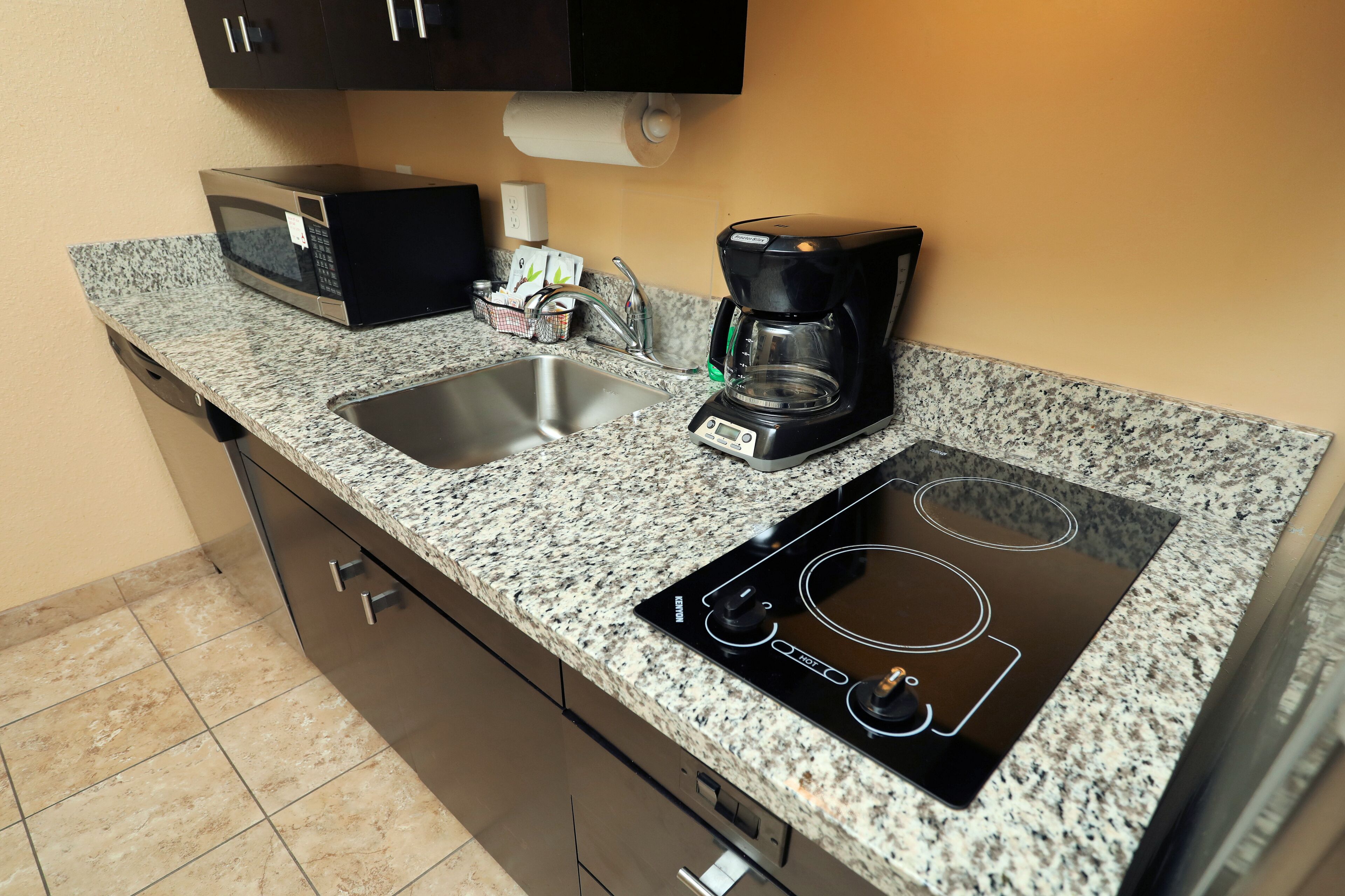 A kitchen with a granite countertop, a microwave, a coffee maker, a sink, and an induction cooktop.