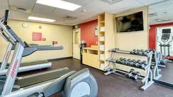 A gym with treadmills, dumbbells, and a television on the wall.