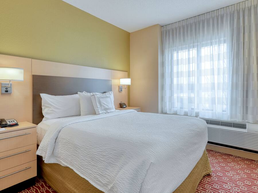 A hotel room with a bed, bedside tables, a telephone, and a window with curtains.