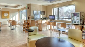 A modern interior with seating areas, a bar, and large windows. - TownePlace Suites York (York)