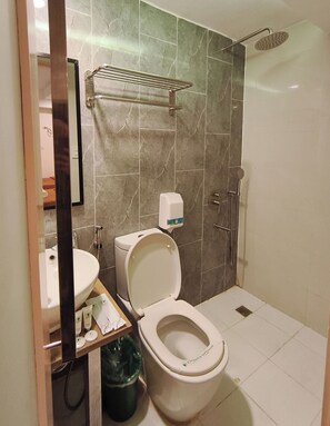 Un baño con inodoro, lavamanos, ducha y perchero para toallas.