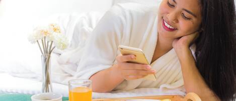 A person lying in bed with a tray of breakfast, a cup of coffee, and a glass of orange juice.