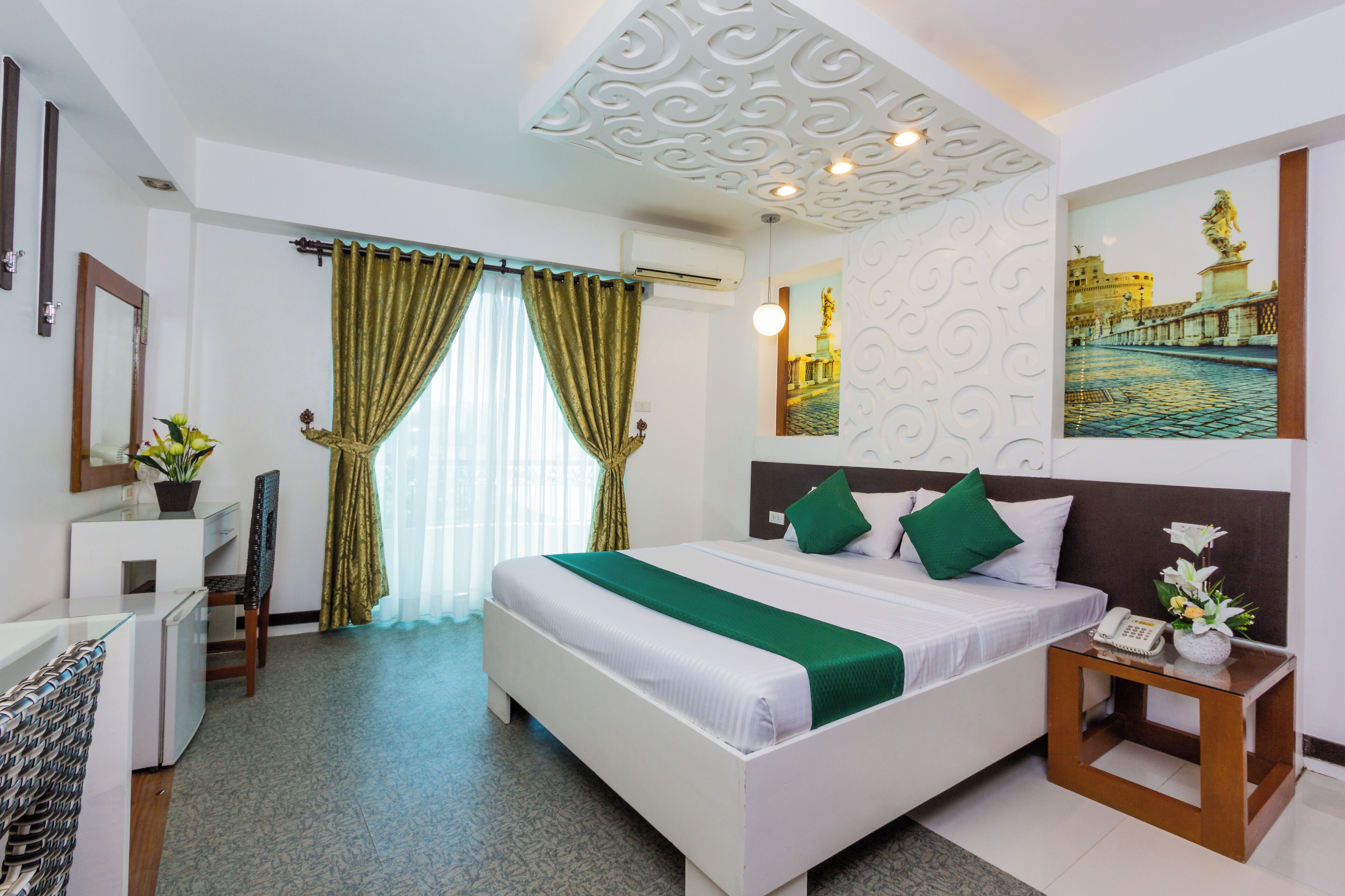 A hotel room with a bed, a desk, a chair, a nightstand, and a wall-mounted phone.