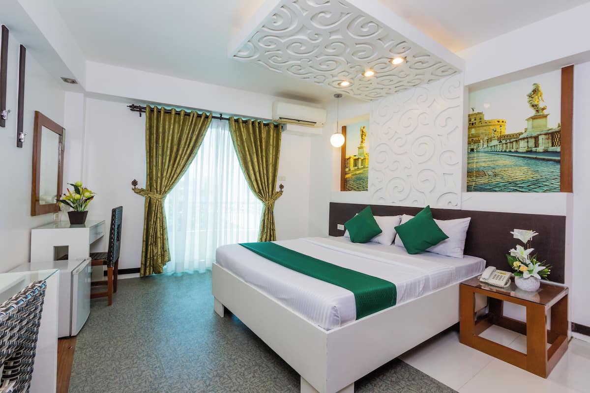 A hotel room with a bed, a desk, a chair, a nightstand, and a wall-mounted phone.