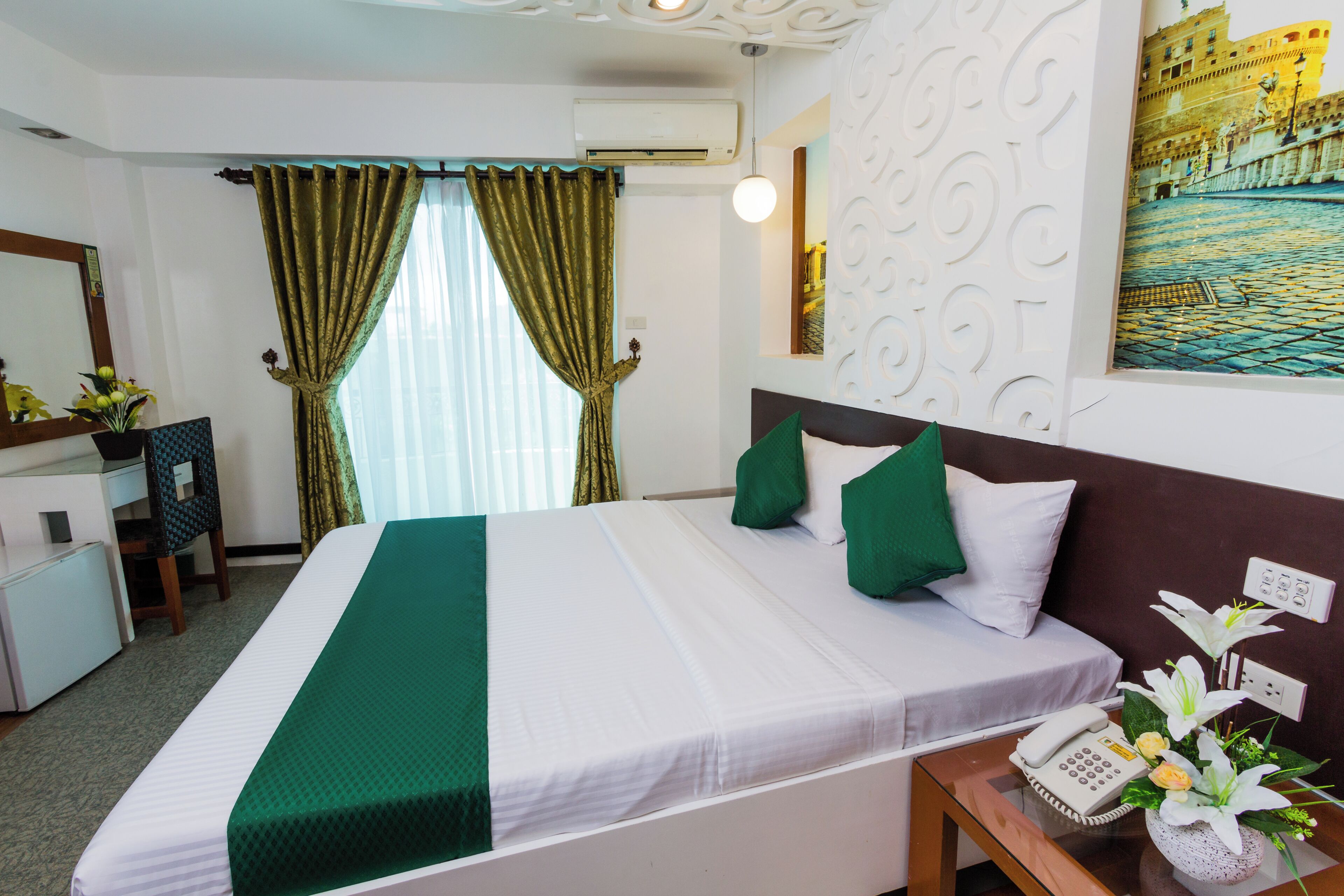 A hotel room with a bed, a desk, a chair, a telephone, and a wall-mounted air conditioner.