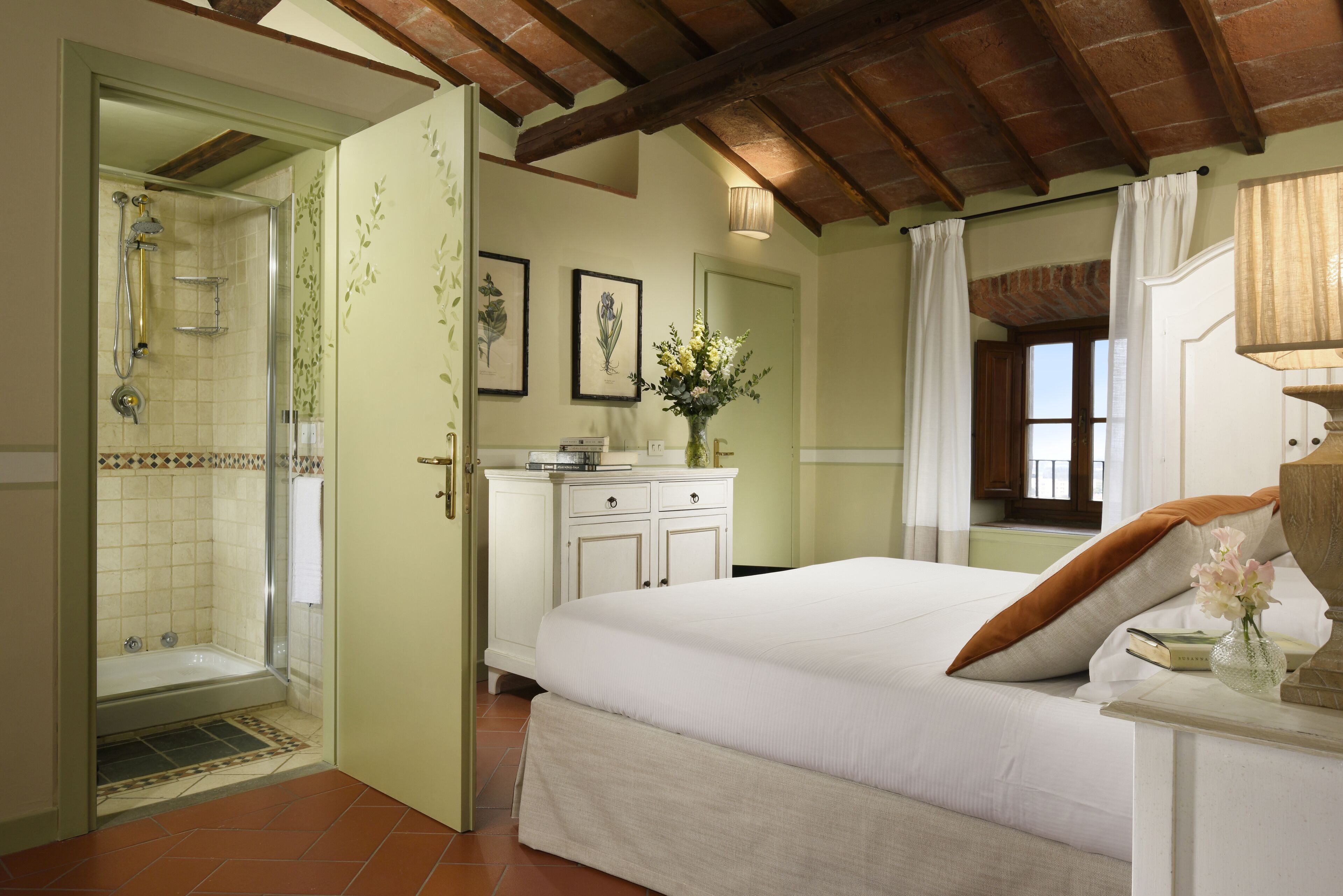 A bedroom with a large bed, a nightstand, a dresser, a shower, and a window with curtains.