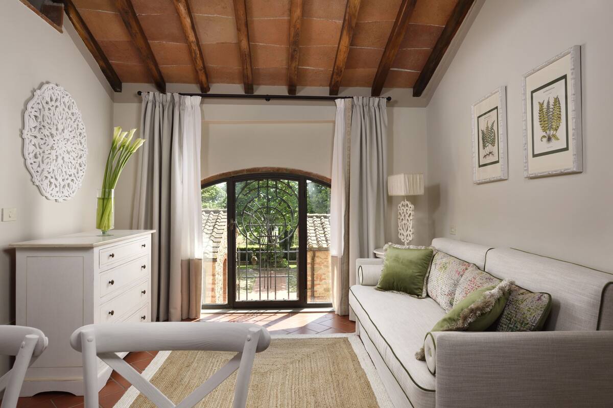Un salon comprenant un canapé, une petite table, un meuble blanc et une vue sur un espace extérieur, accessible par une porte vitrée.