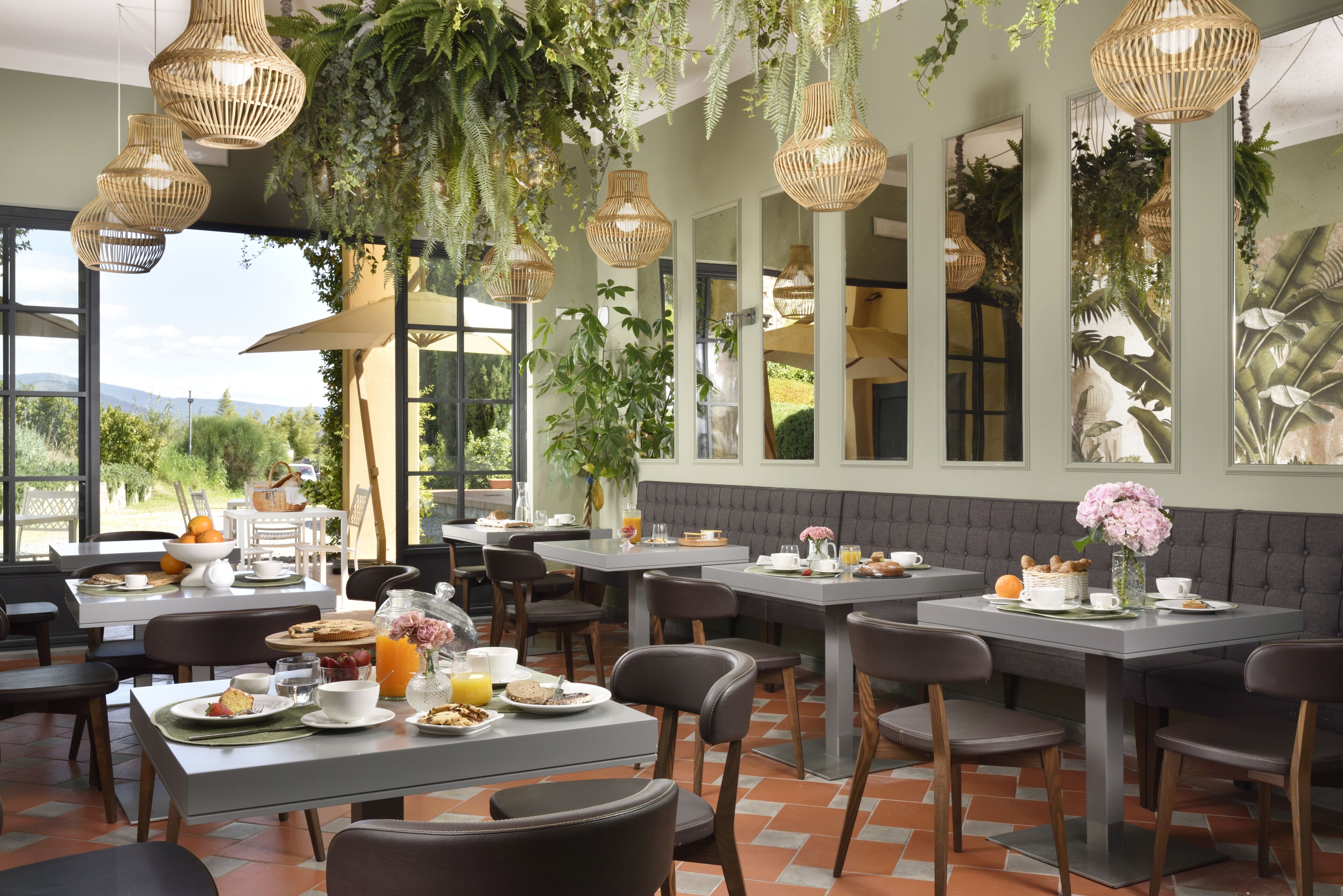 Un restaurant doté de nombreuses tables et chaises, de grandes fenêtres et de plantes suspendues.