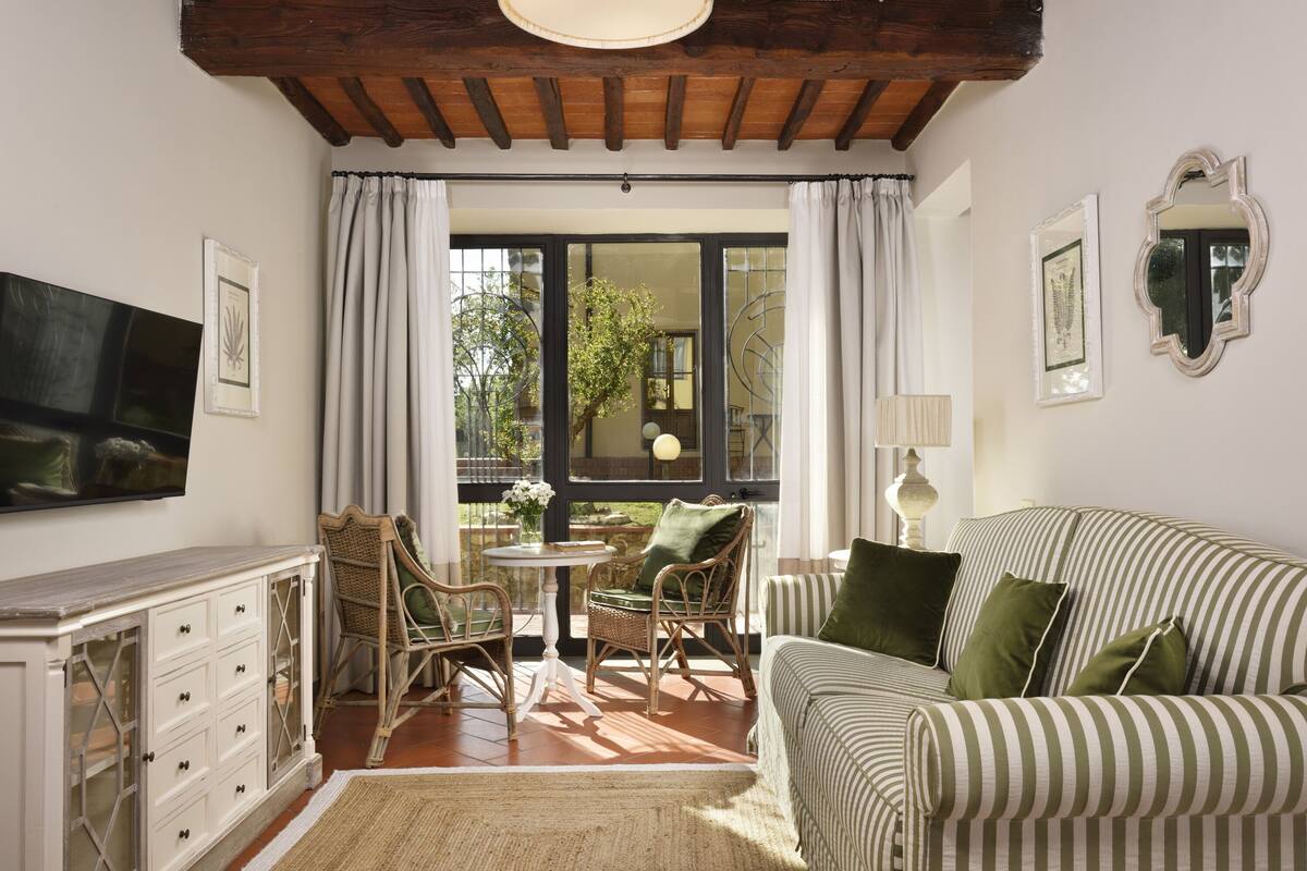 Un salon chaleureux avec un canapé à rayures, des fauteuils en osier, une petite table et un téléviseur fixé au mur.