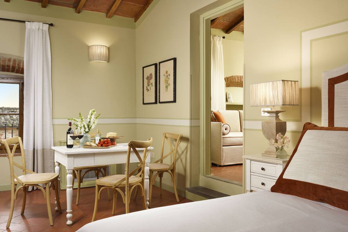 Une chambre à coucher comprenant un lit, une table de chevet, une commode, une chaise, un bureau et une fenêtre avec des rideaux.