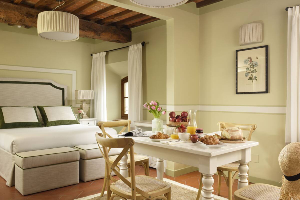 Une pièce bien éclairée, avec un lit, une table pour le petit-déjeuner, des chaises et un tableau encadré au mur.