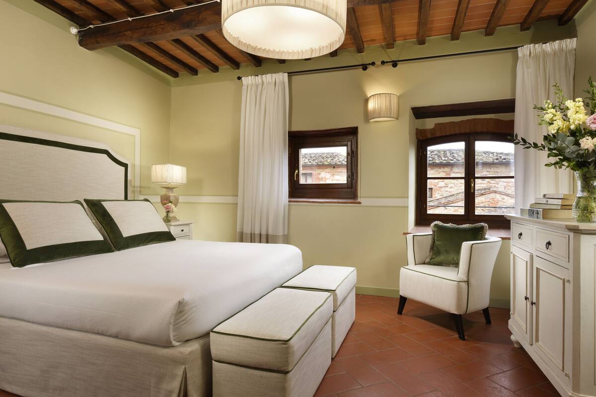 Une chambre à coucher avec un grand lit, une chaise, une table de chevet, une lampe, une fenêtre et une armoire.