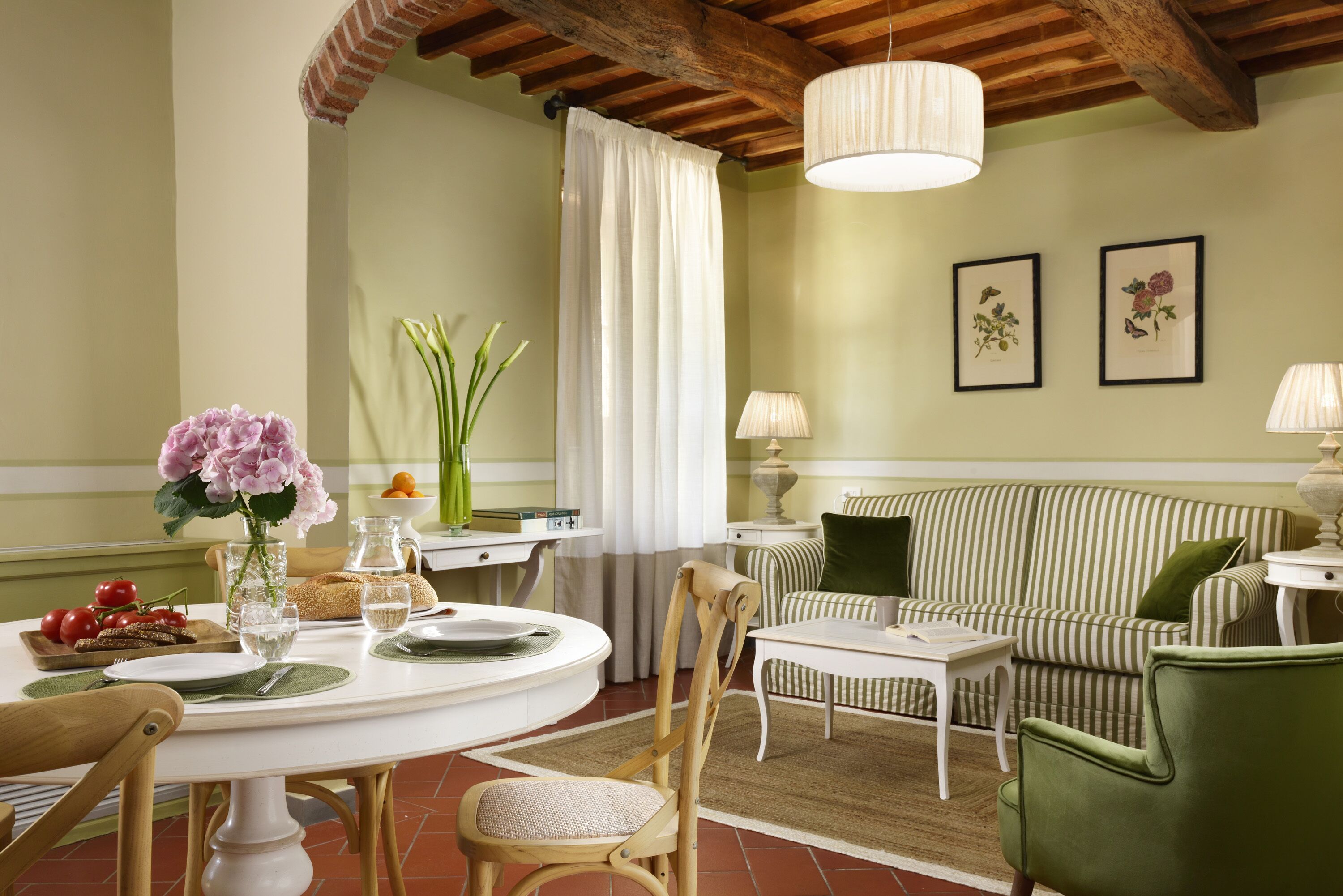 Un comedor con una mesa redonda, sillas, un jarrón de flores y un sofá al fondo.