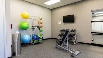 Un gimnasio con equipo de ejercicio, un televisor y un espejo.