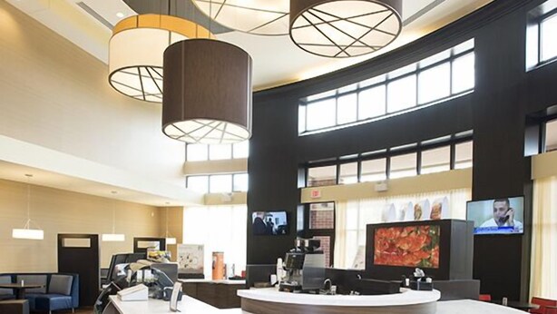 A modern bar area with a curved counter, multiple stools, and pendant lighting. - Courtyard Cincinnati Midtown/Rookwood (Cincinnati)
