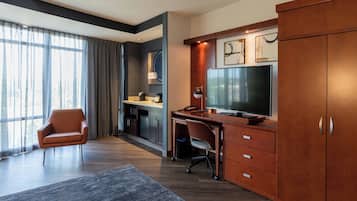 Habitación de hotel moderna con un escritorio grande, televisor y una silla cómoda.