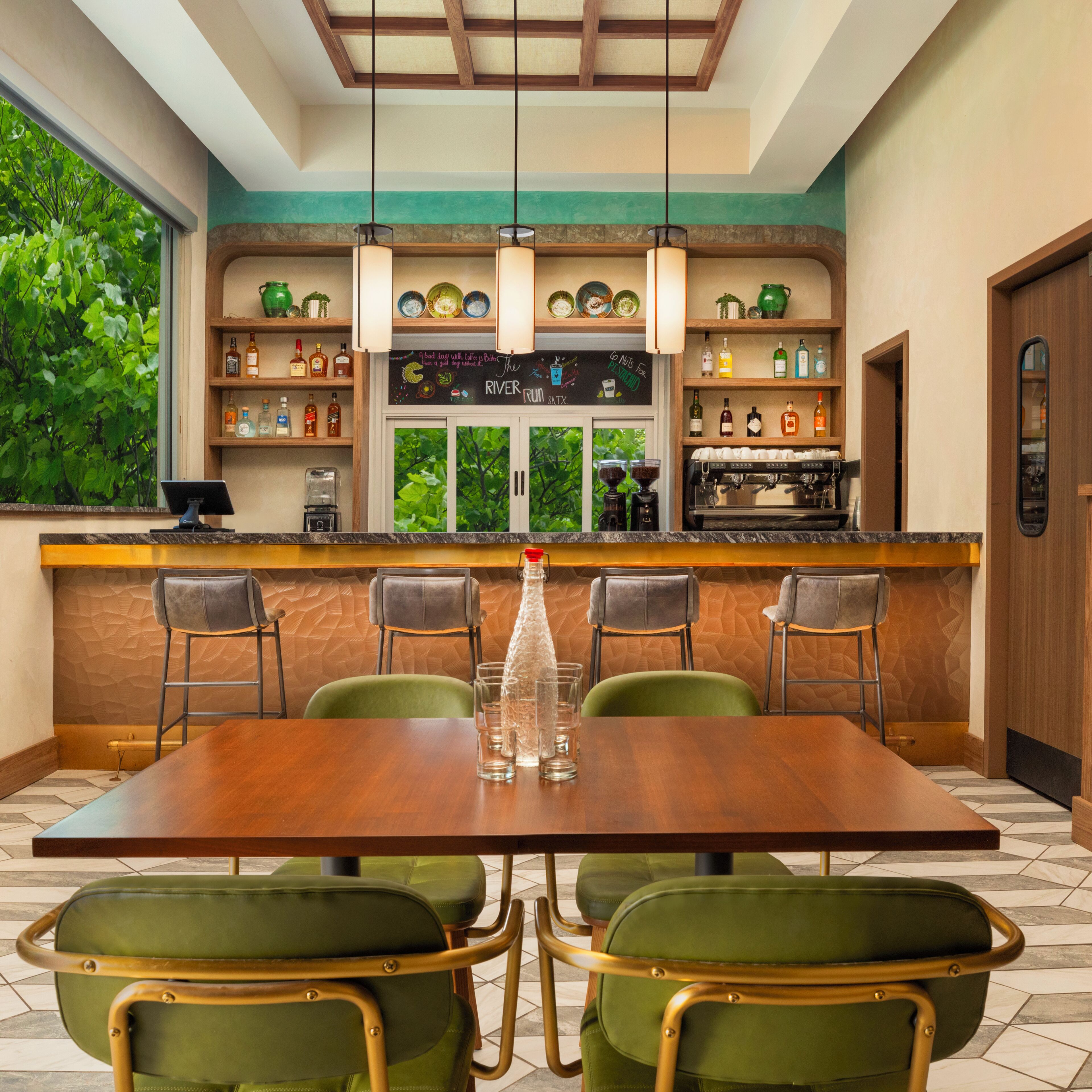 A restaurant with a wooden bar, green chairs, and a coffee machine.