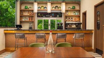 A restaurant with a wooden bar, green chairs, and a coffee machine.