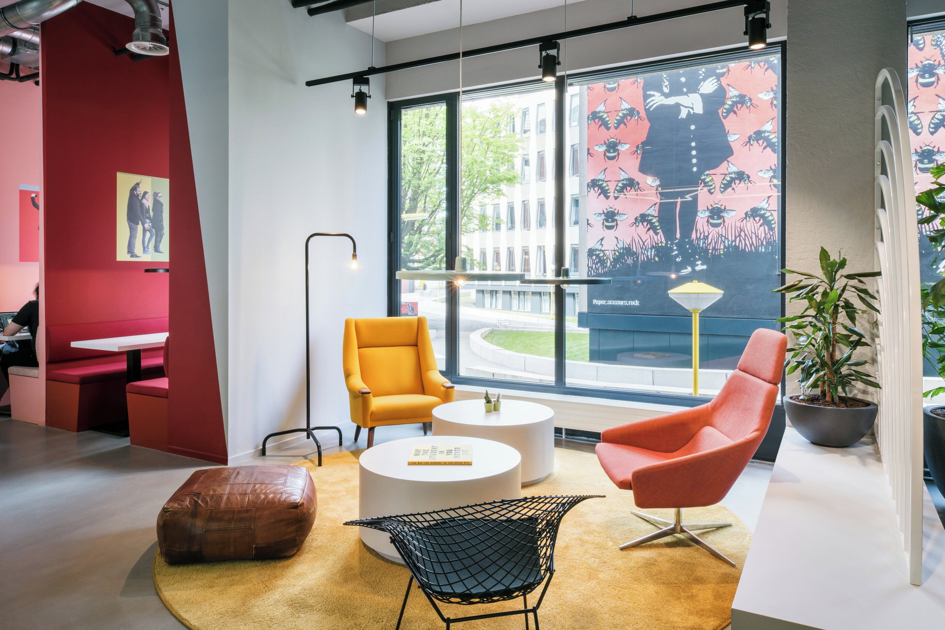 Un intérieur moderne avec un mur d’accent rouge, des chaises jaunes et rouges, une table basse ronde et une grande fenêtre donnant sur la ville.