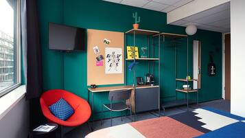 A modern room with teal walls, a red chair, a desk, a TV, and a bookshelf.