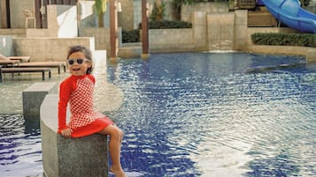 A child sitting by a pool with a slide in the background.