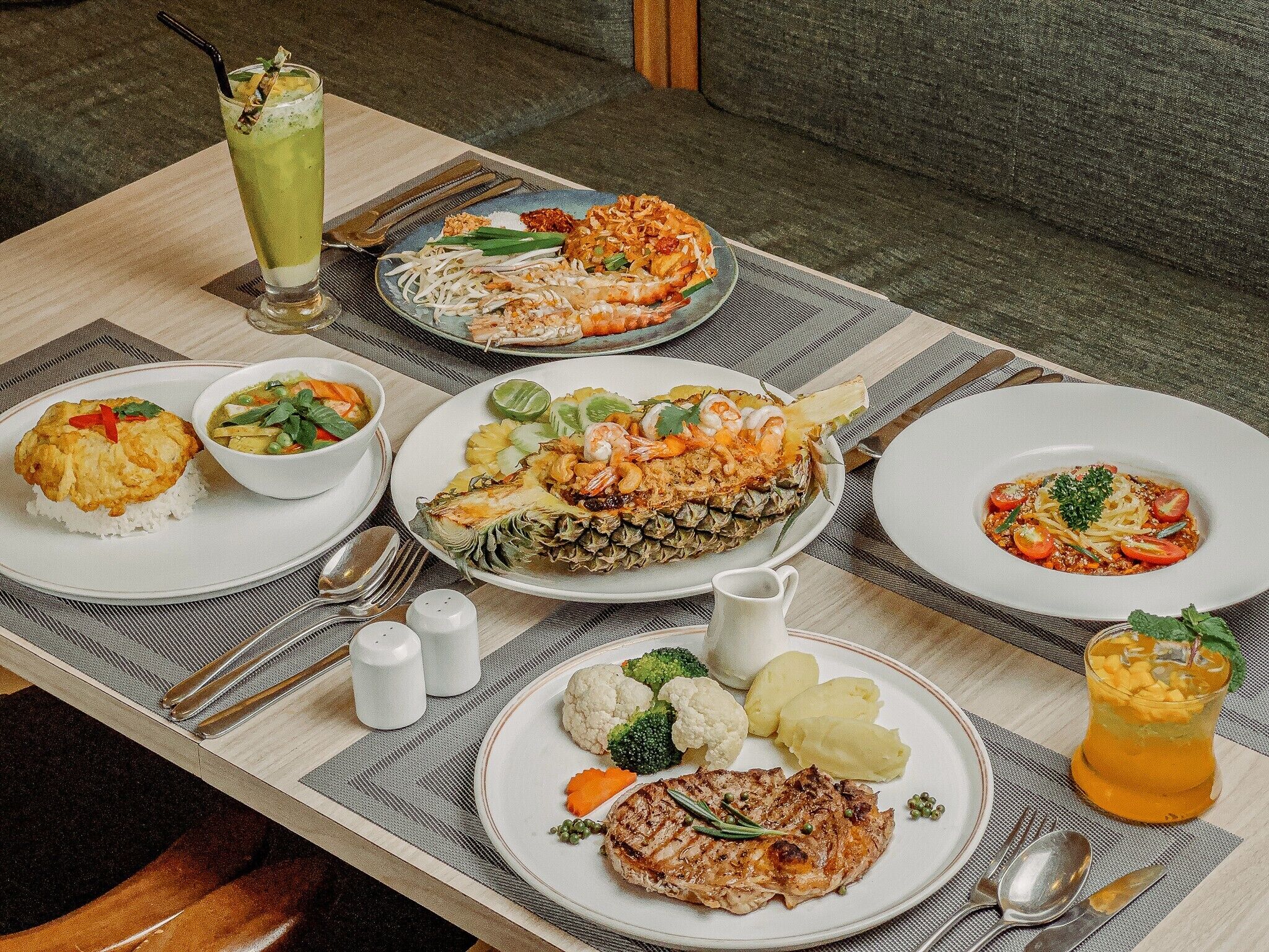 A table set with various dishes including a grilled steak, a pineapple salad, and a bowl of soup.