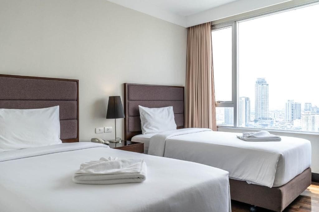 Een hotelkamer met twee bedden, uitzicht op de stad en een raam met gordijnen.