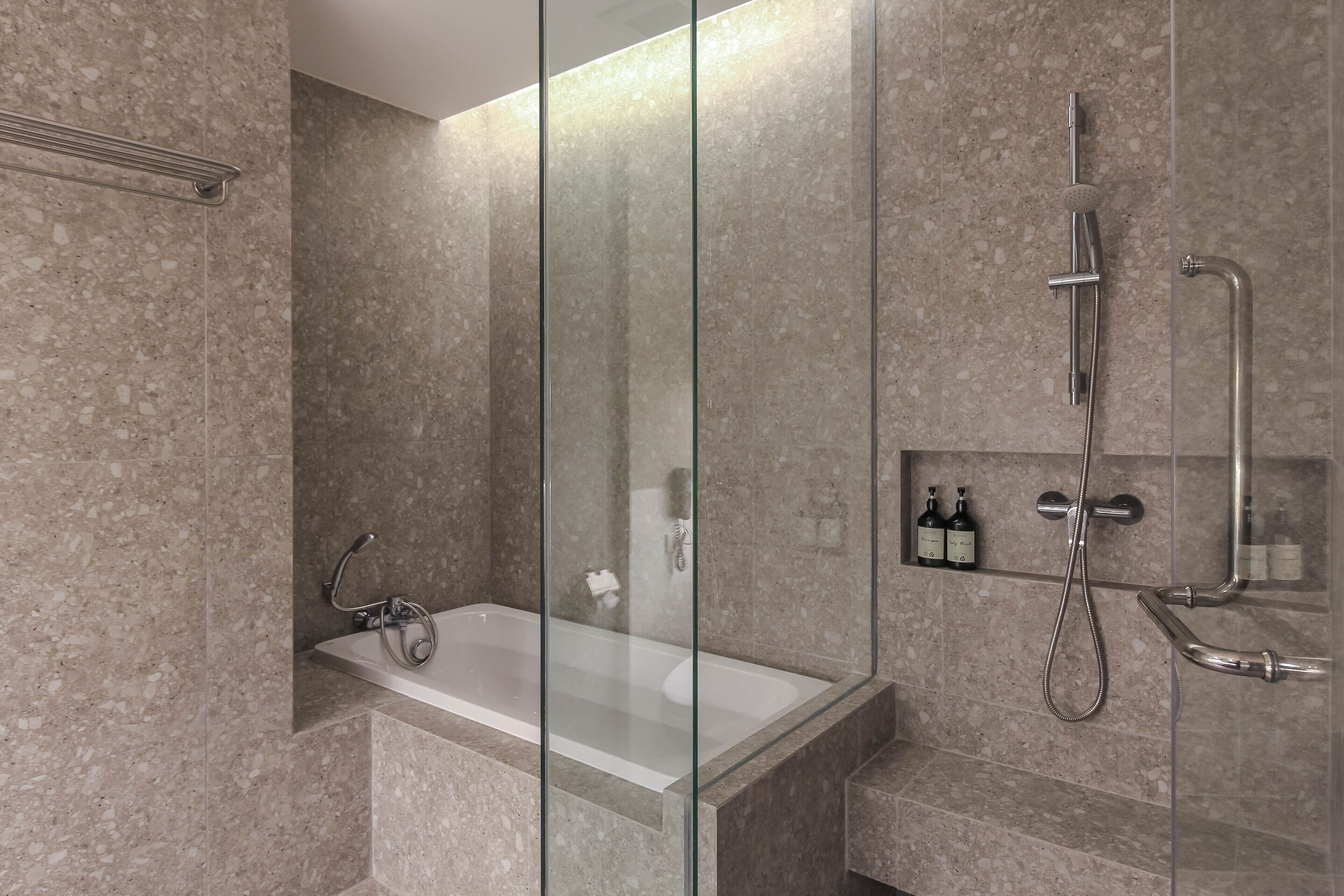 A modern bathroom with a glass-enclosed shower, a bathtub, and a shelf with toiletries.