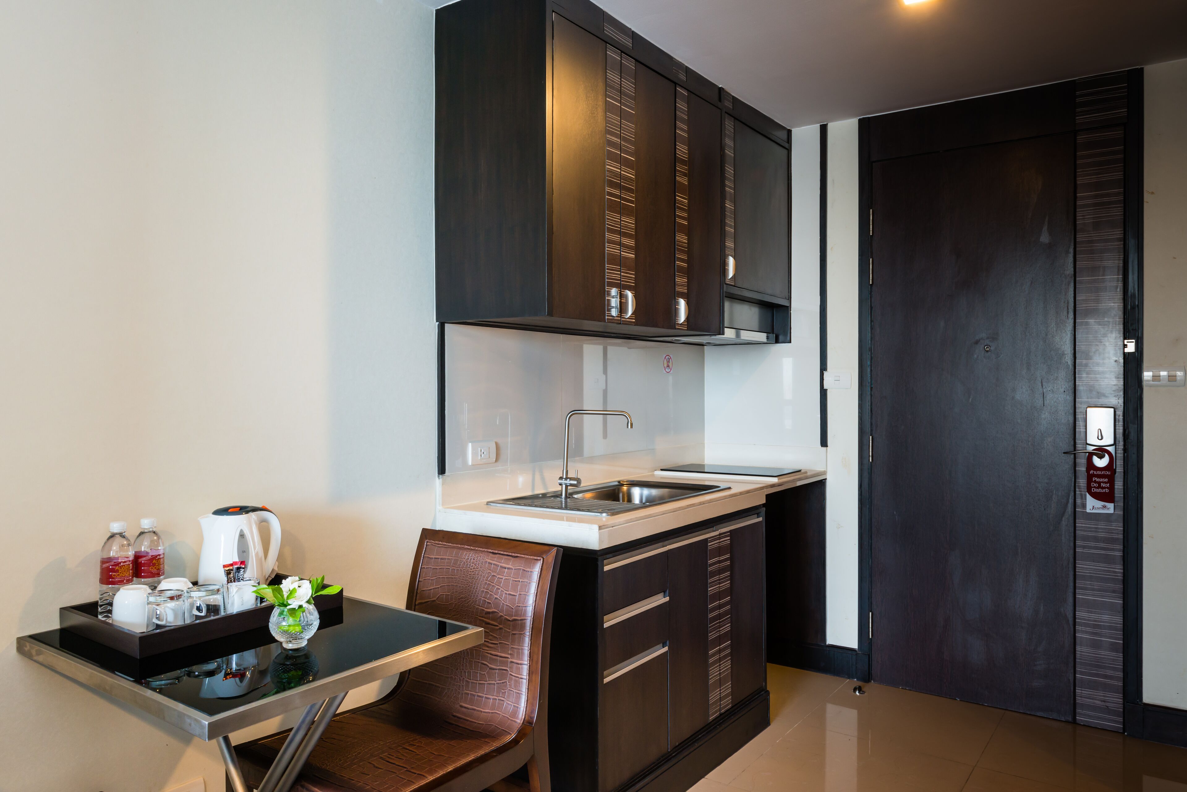 A compact kitchen with dark cabinetry, a stainless steel sink, and a small dining area with a table and chair.