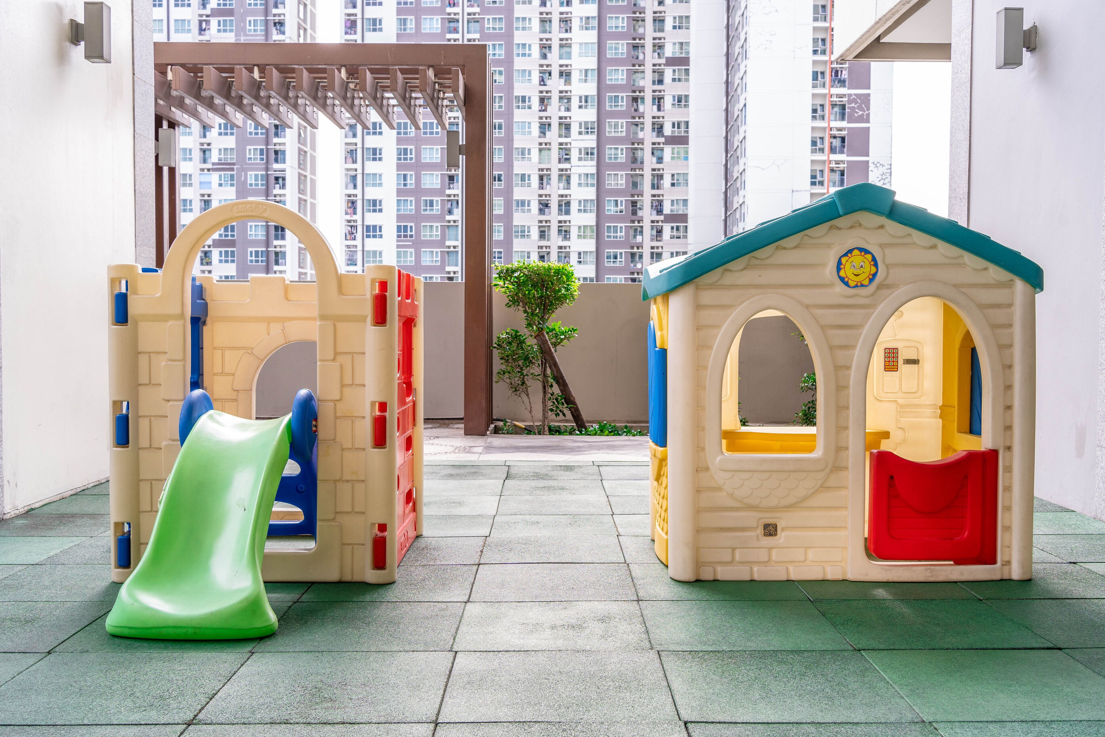Zona infantil con tobogán y una casita, frente a edificios altos.