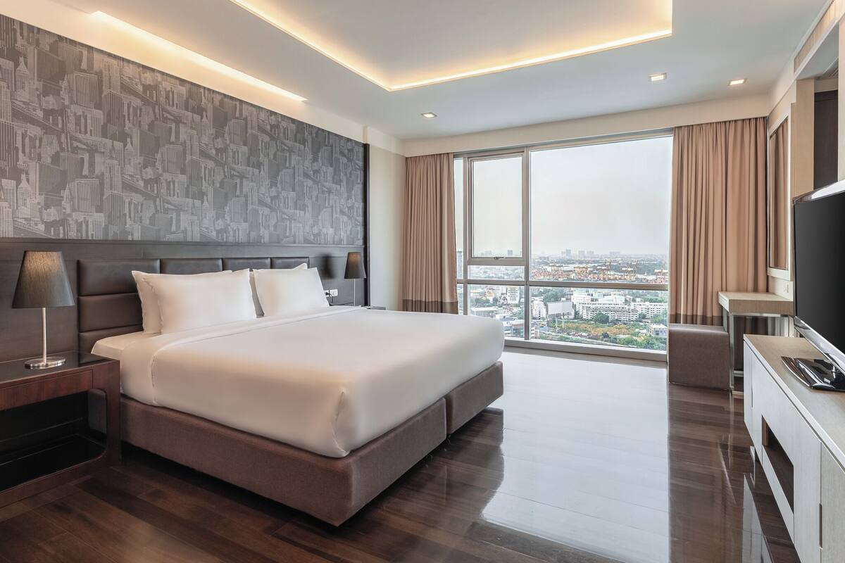A modern hotel room with a large bed, a city view, and a flat-screen TV.