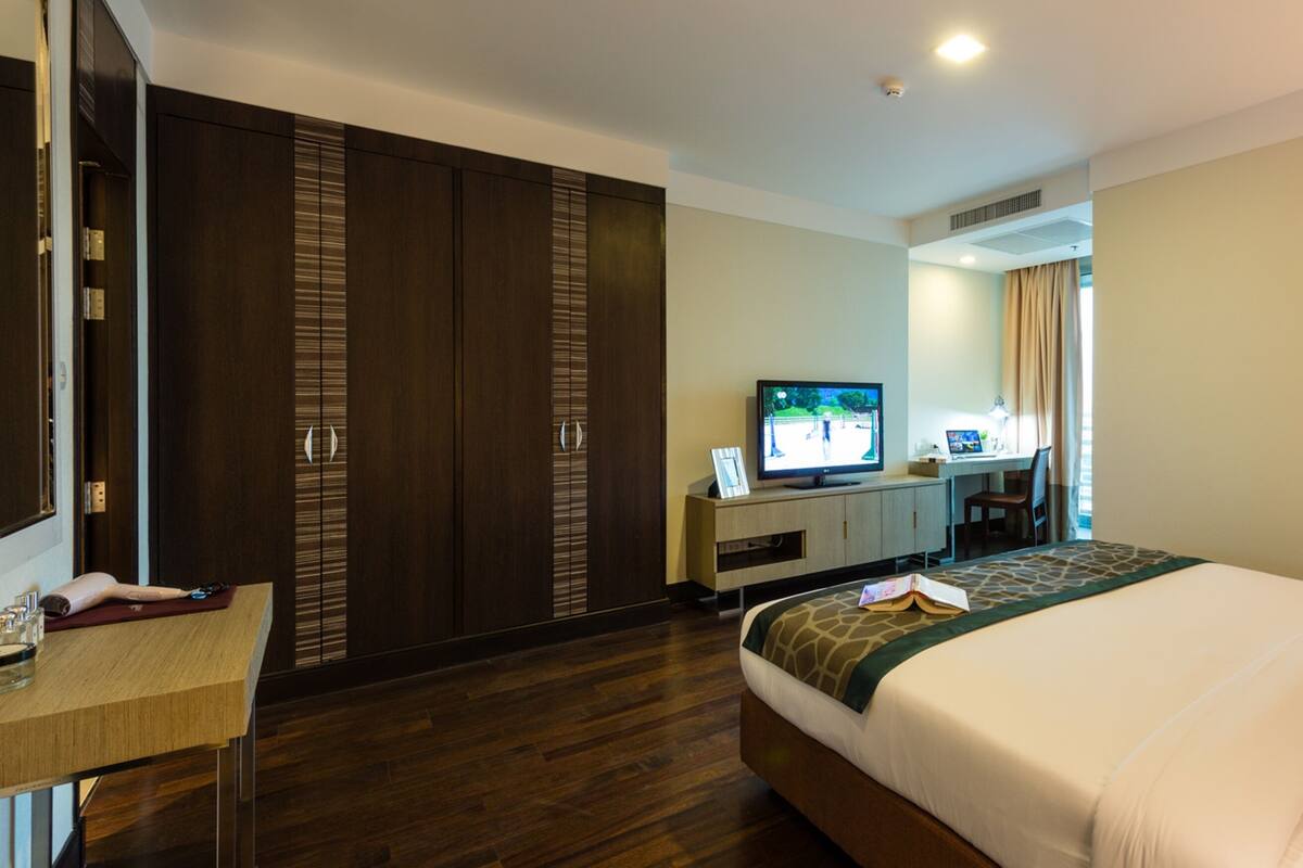 A hotel room with a bed, a desk with a computer, a television, and a wardrobe.