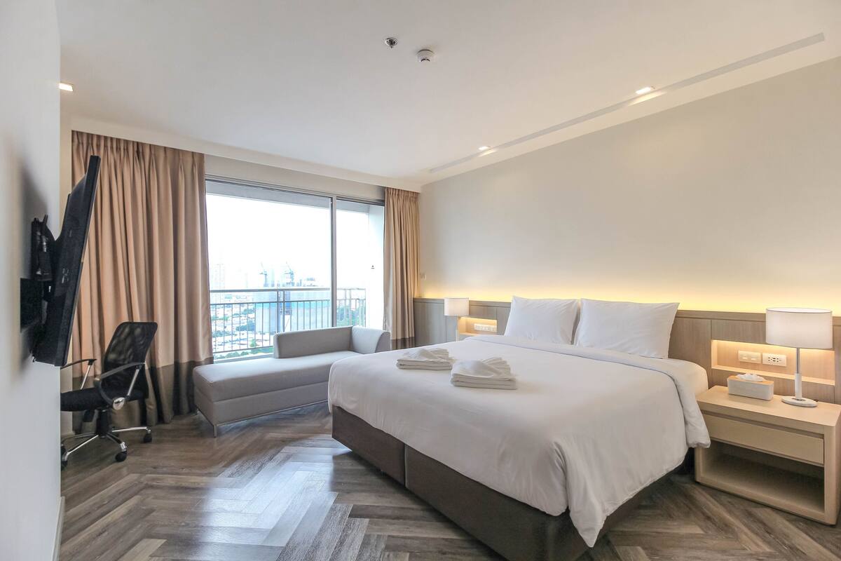 A hotel room with a large bed, a desk, a chair, and a window with curtains.