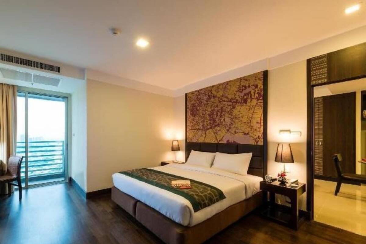 A hotel room with a large bed, a view of the ocean, a map artwork on the wall, and a chair by the window.