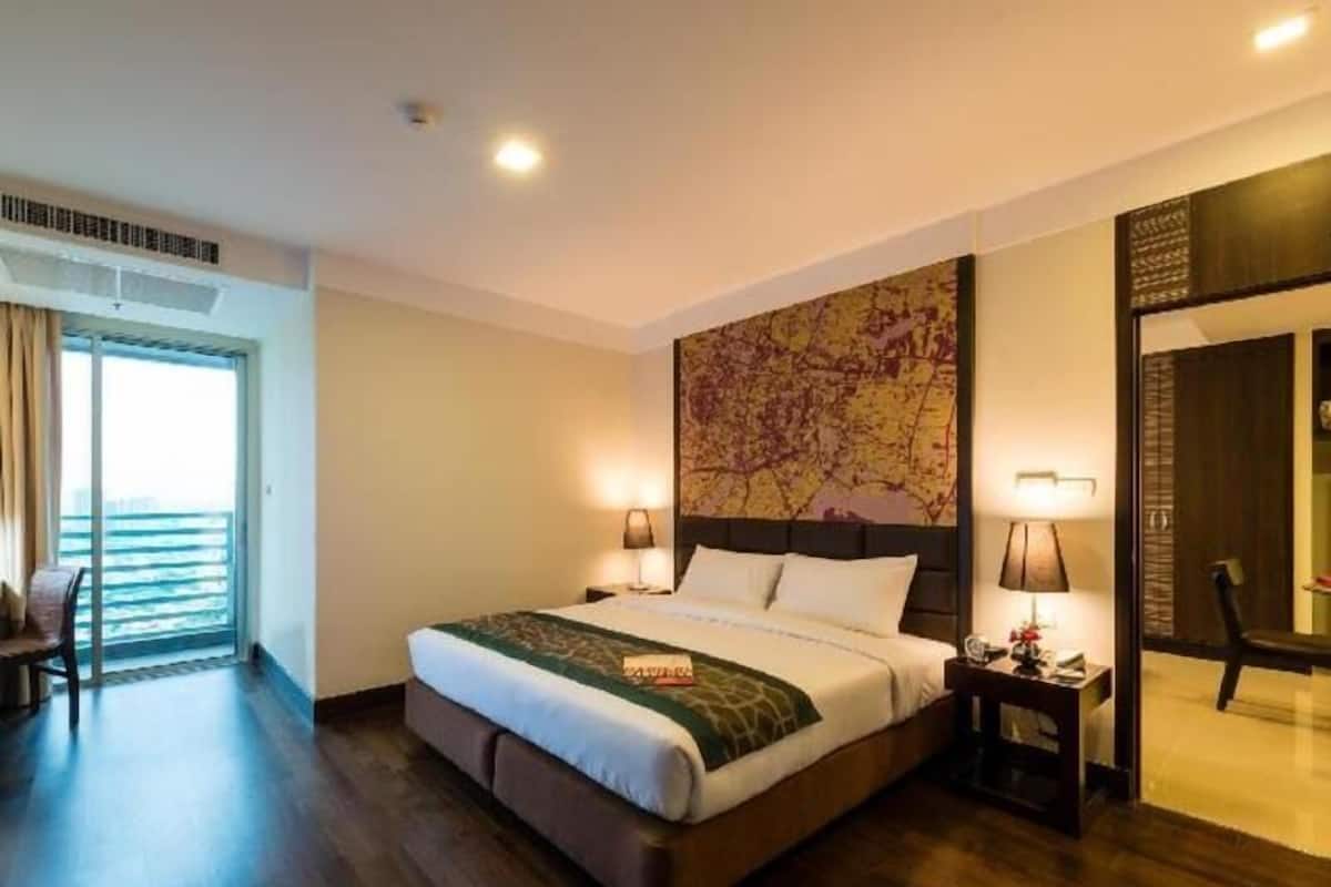 A hotel room with a large bed, a view of the ocean, a map artwork on the wall, and a chair by the window.