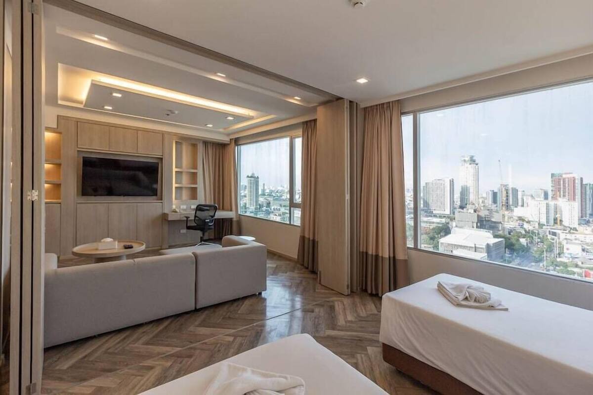 A modern hotel room with a large bed, a sofa, a TV, and a city view.