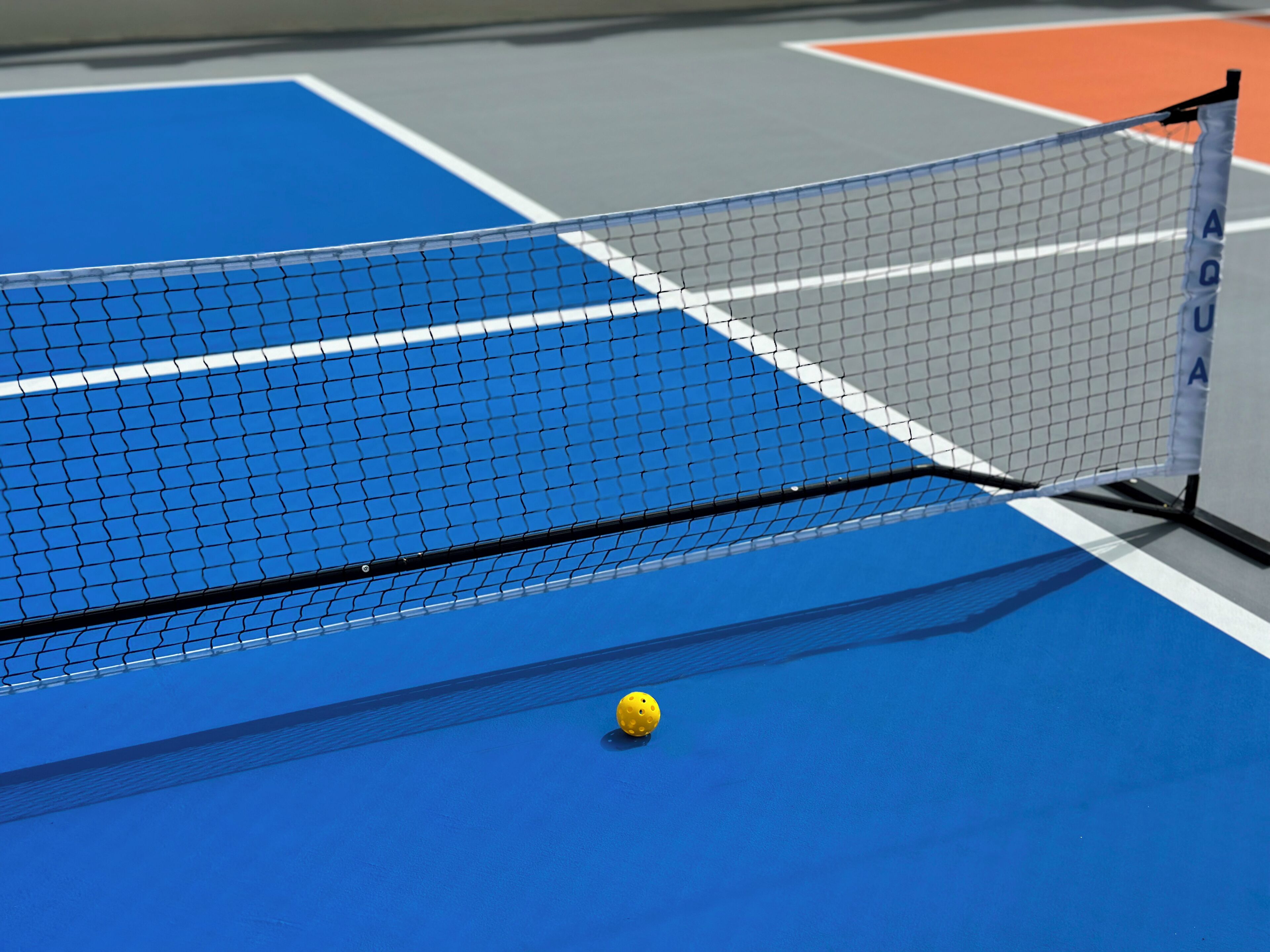 A tennis court with a net labeled "AQUA" and a yellow tennis ball on the court.