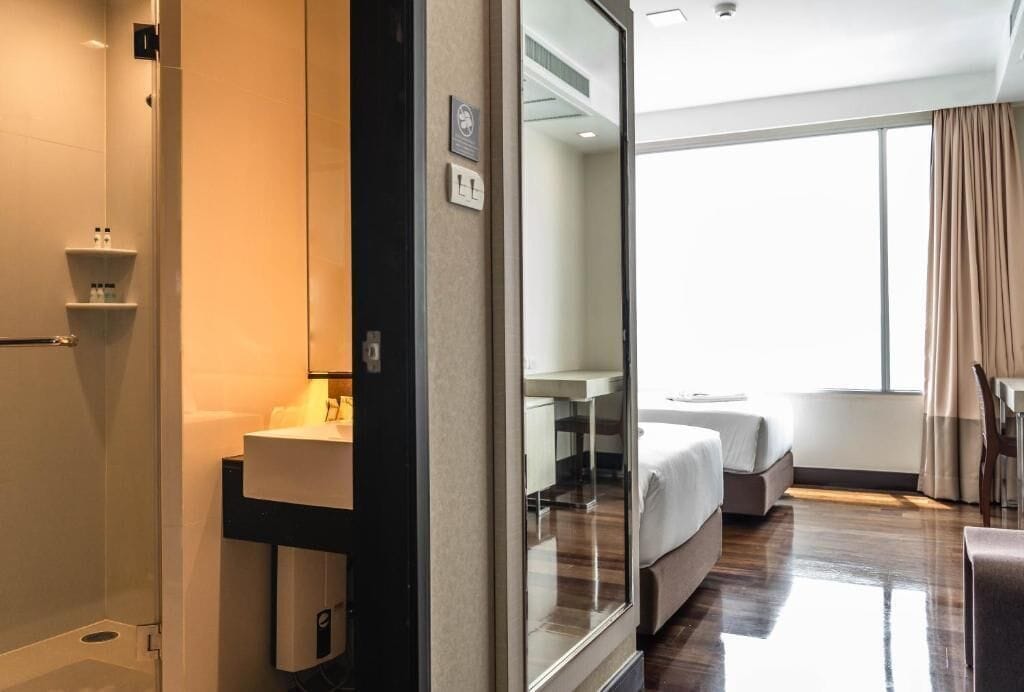 A hotel room with a large mirror, a bed, a bedside table, and a window with curtains.