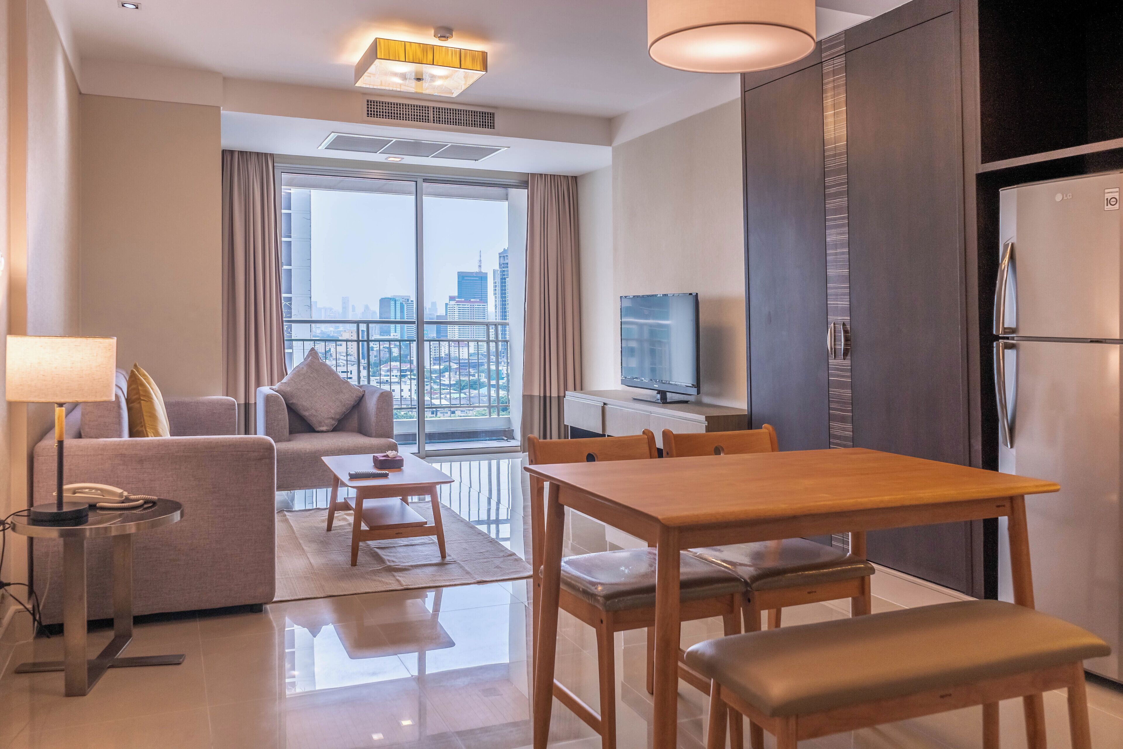 Una habitación de hotel moderna con balcón, zona de comedor, sofá, televisor y refrigerador.