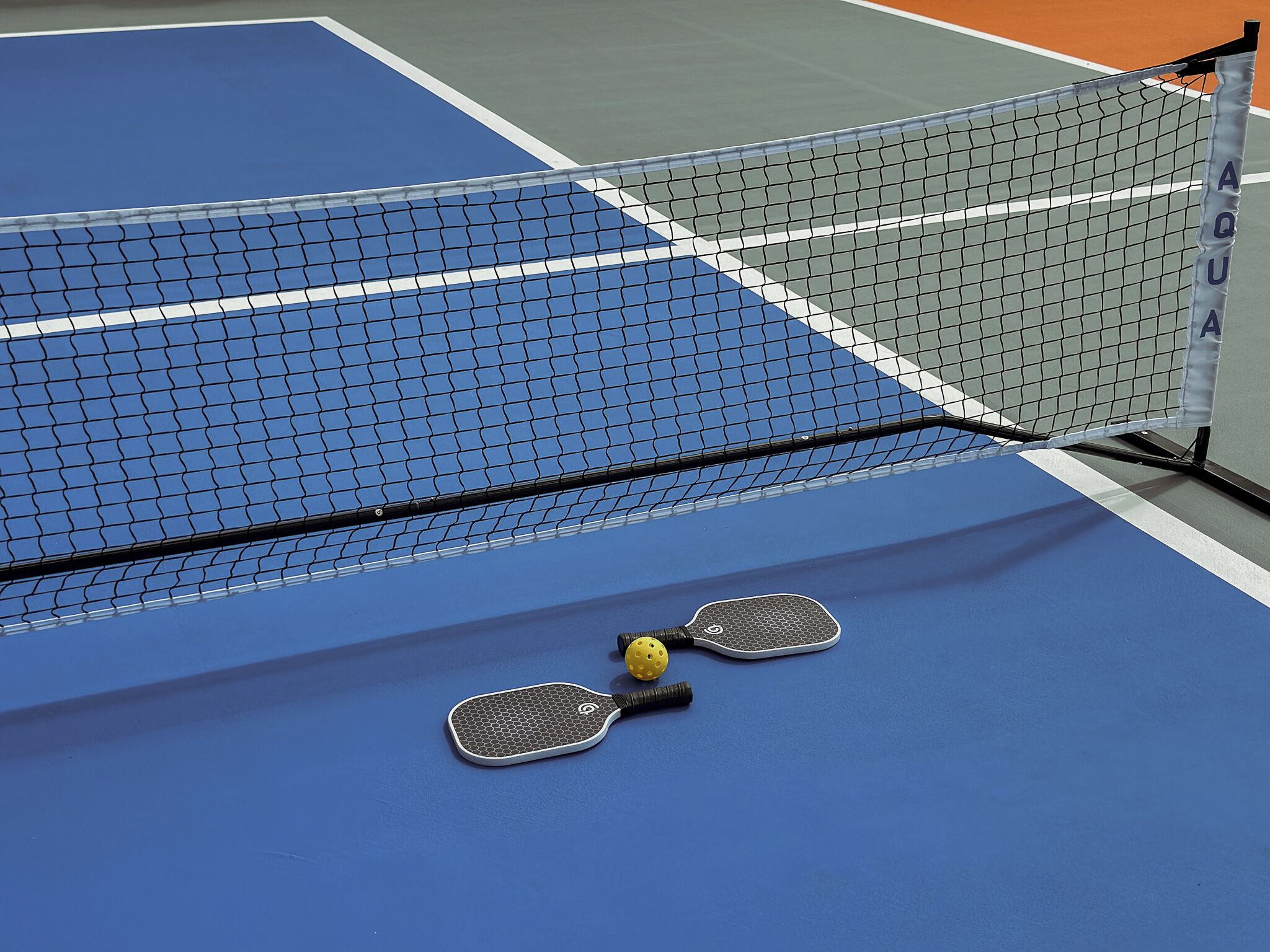 Una cancha de tenis con una red, dos raquetas y una pelota de tenis.