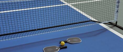 Una cancha de tenis con una red, dos raquetas y una pelota de tenis.