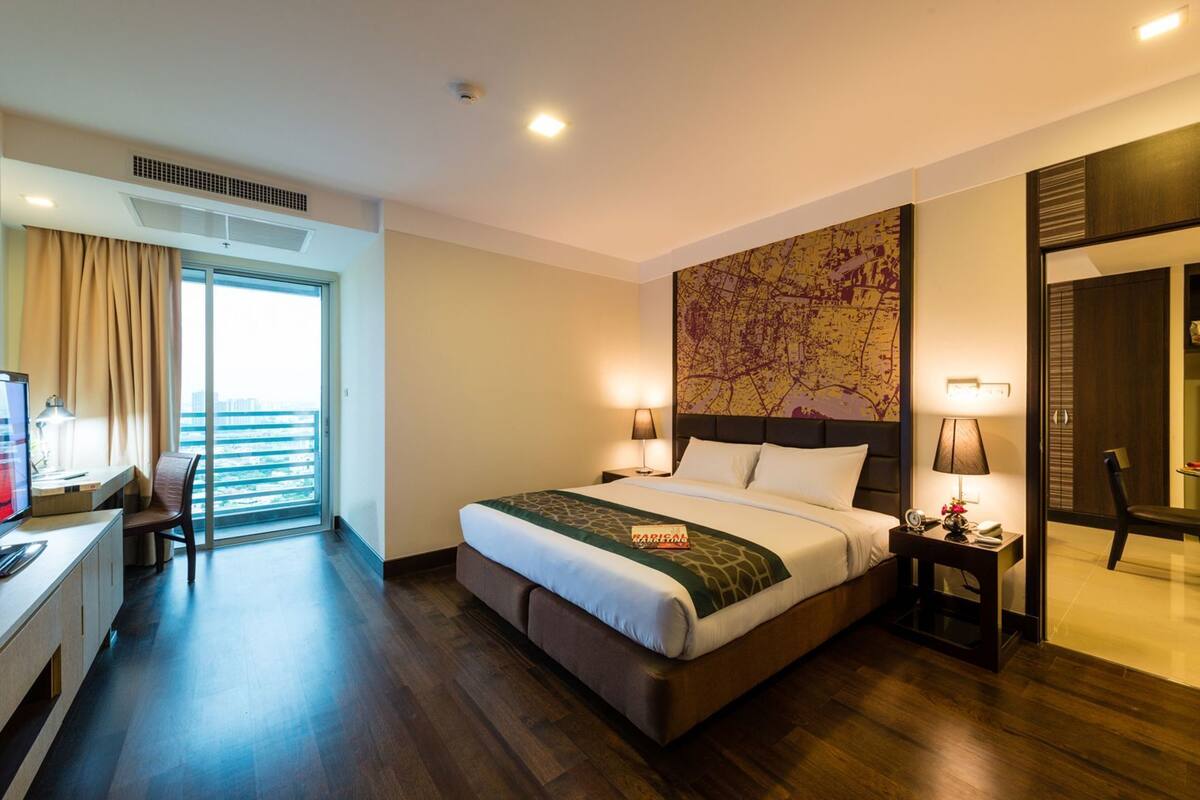 A hotel room with a bed, desk, and chair, a large window, and a map on the wall.