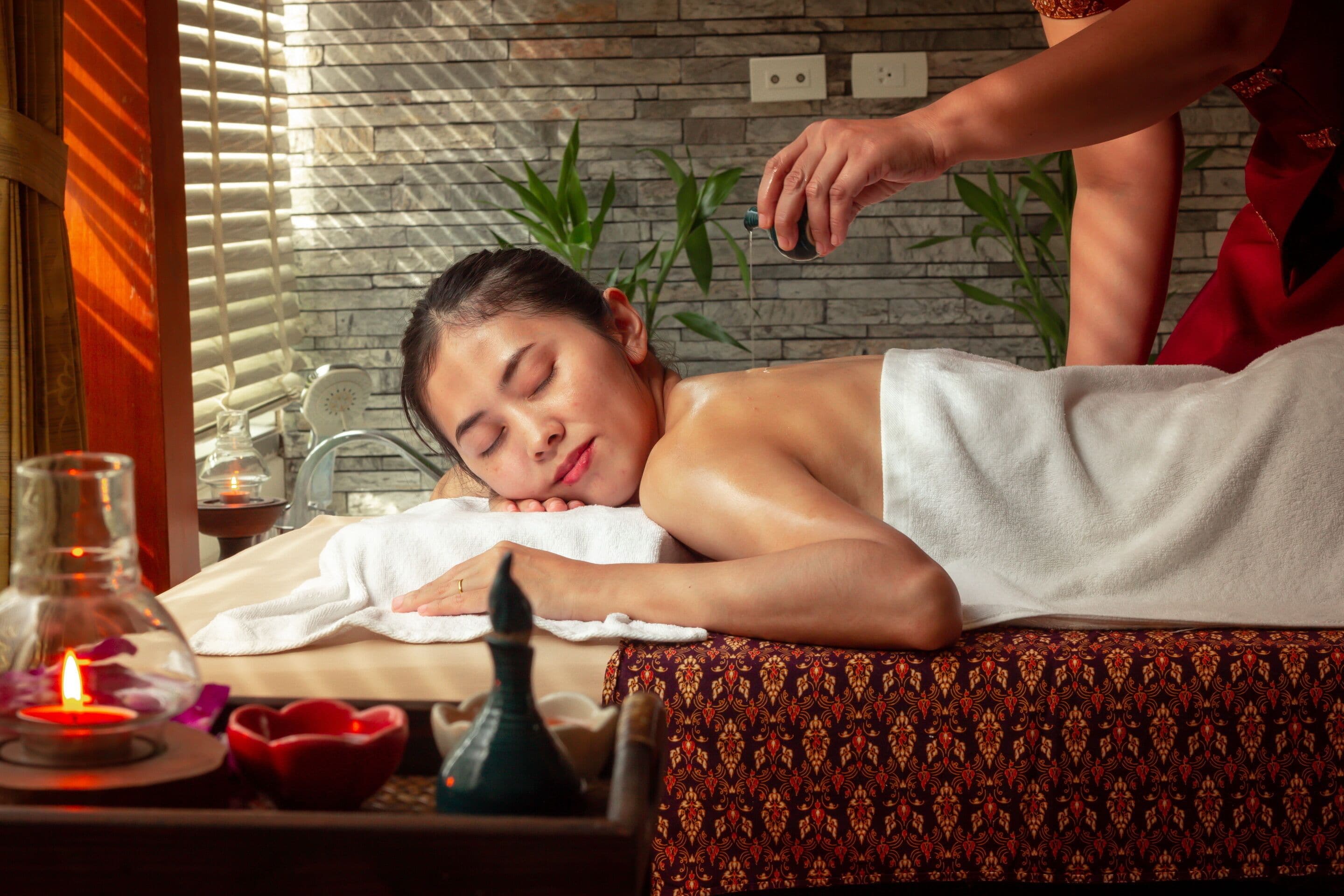 A massage therapy session in a spa setting with a stone wall, a massage table, and a candle.