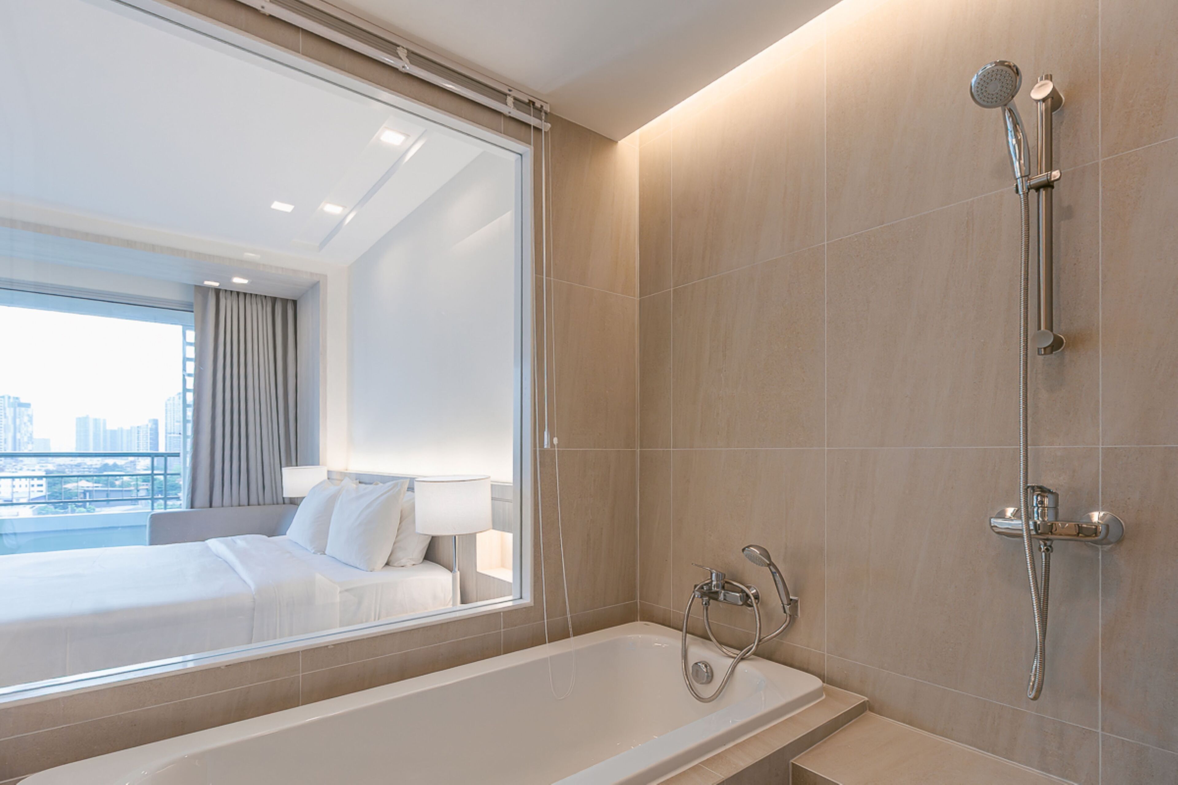 A modern hotel bathroom with a bathtub, a shower, and a large window offering a city view.