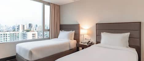 Habitación de hotel con dos camas, vistas a la ciudad, una ventana con cortinas y una mesita de noche con lámpara.