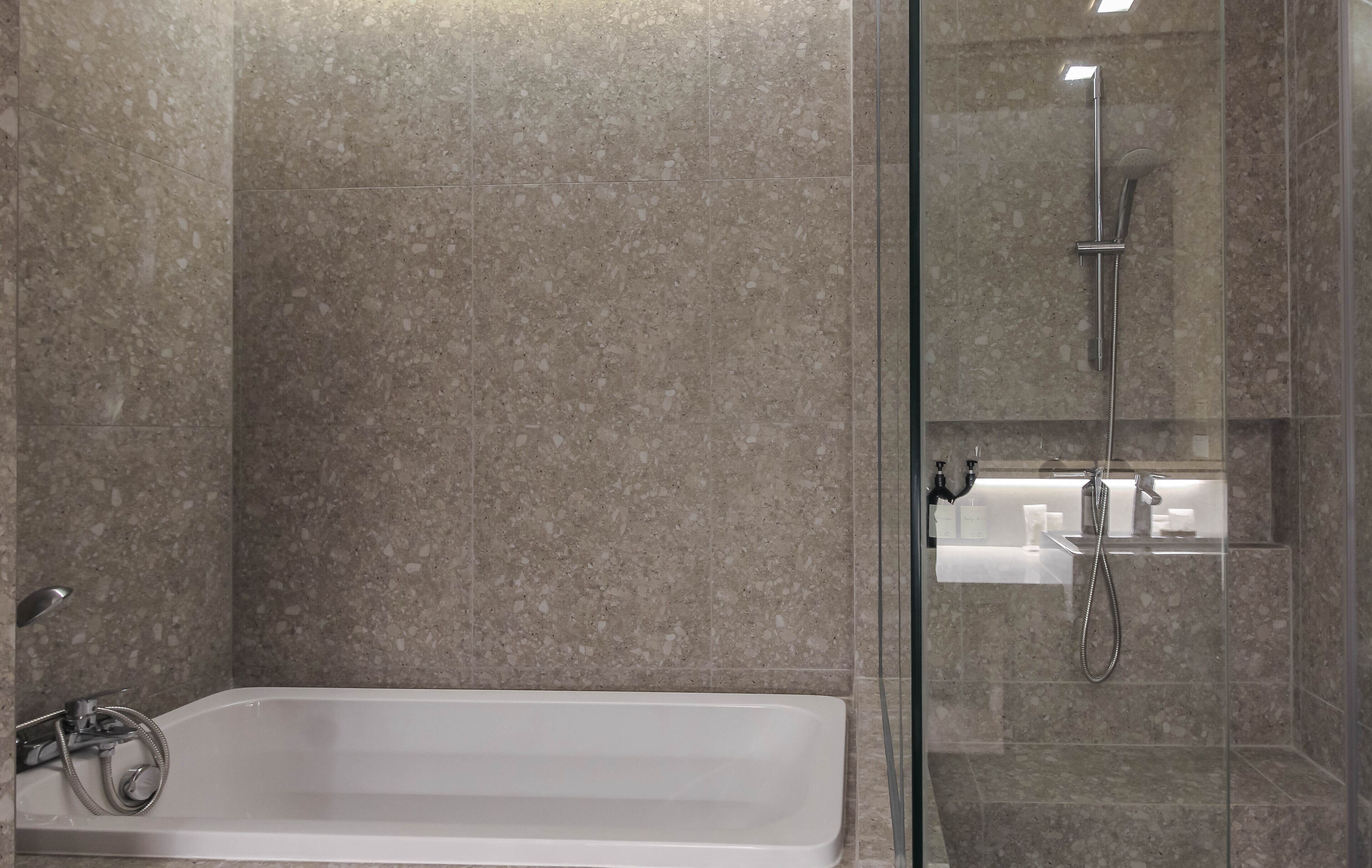 A modern bathroom with a glass-enclosed shower, a standalone bathtub, and a marble-tiled wall.
